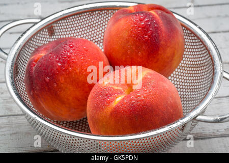Peaches with morning dew in a stainless steel colander isolated on a white surface. Sharp focus set to front peach. Stock Photo