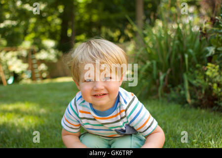 young happy toddler boy smiling and sitting in grass Stock Photo