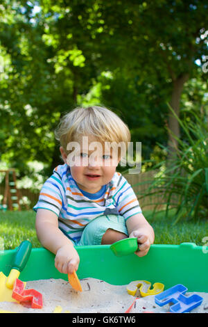 young happy toddler boy smiling and playing in sandbox Stock Photo