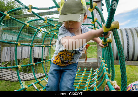 A young boy plays on a climbing net at a children's playground with a helping hand from his Mum. Stock Photo