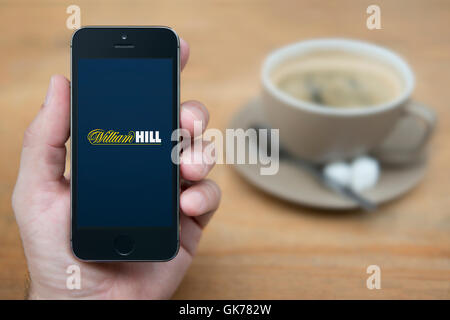 A man looks at his iPhone which displays the William Hill logo, while sat with a cup of coffee (Editorial use only). Stock Photo