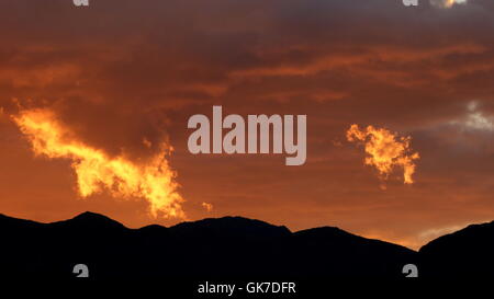 Desert mountain sunset leaves several clouds lit up in golden colors Stock Photo