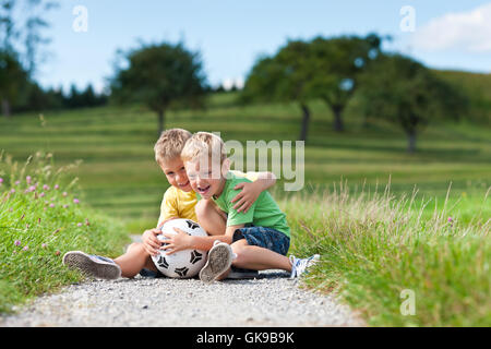 two children with football sitting on a dirt road Stock Photo