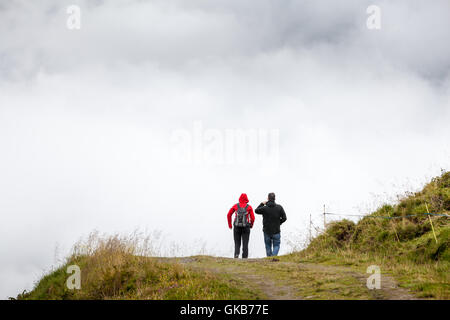 people from behind walking on a mountain track in front of a dense fog wall Stock Photo