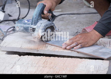 worker cutting a tile using an angle grinder at construction site Stock Photo