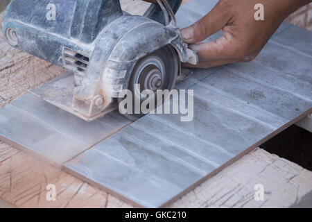worker cutting a tile using an angle grinder at construction site Stock Photo