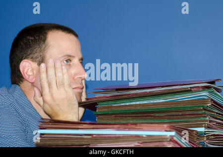 Man with head in hand looking out dreaming of the weekend while work is piling up in front of him. Stock Photo
