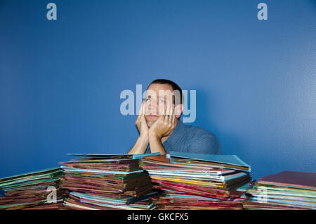 Young man at desk with hands on his cheeks stressed out by all the files in front of him. Stock Photo