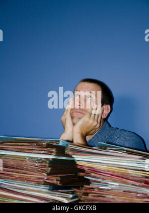 Man hiding behind piles files looking up at the ceiling. Example of an overworked, overwhelmed employee. Stock Photo