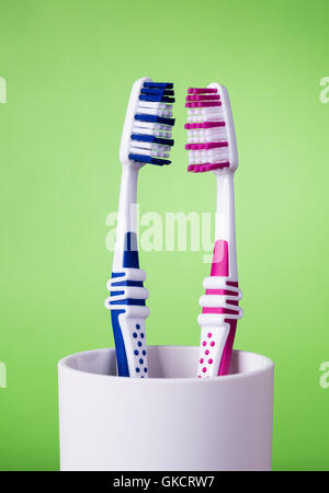 Two toothbrushes in white cup on green background. The toothbrushes are in vertical position. Stock Photo