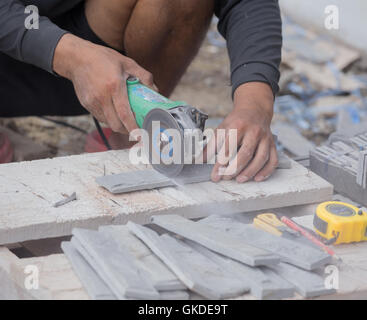 worker cutting a sand stone tile using an angle grinder at construction site Stock Photo