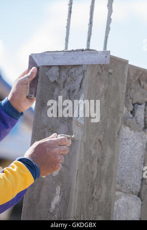 worker use iron ruler snd trowel plastering the poles at construction site Stock Photo