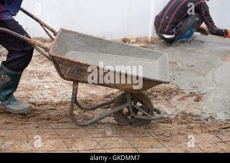 Construction worker pushing barrow with wet cement to pouring concrete floor Stock Photo
