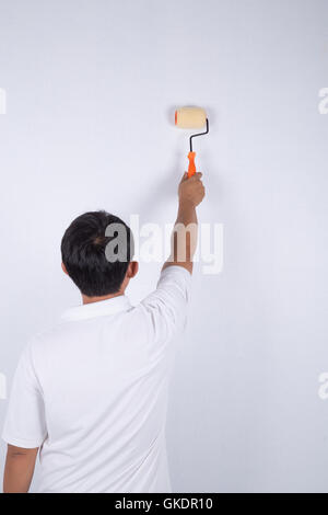 painter man at work with a paint roller on wall background Stock Photo