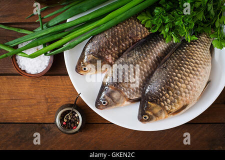 Three fresh raw crucian on a wooden background with herbs. Top view Stock Photo