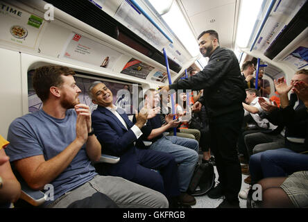 Mayor of London Sadiq Khan (seated 2nd left) applauds poet Hussain Manawer (centre) after he recited his poem The Night Tube, whilst travelling with passengers on a northbound Victoria line tube train during the launch of London's Night Tube, as trains will operate overnight on Fridays and Saturdays on the Victoria line and parts of the Central line, with the Jubilee, Northern and Piccadilly lines following in the autumn. Stock Photo