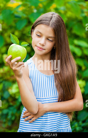 Happy brunette little girl with green apple, summer outdoors Stock Photo