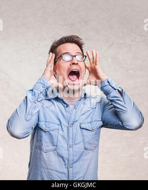Portrait of a shocked, screaming, stunned or surprised young man holding head with his hands - isolated on light gray background Stock Photo
