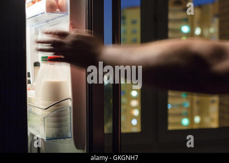 hand reaches for milk bottle in home fridge in night Stock Photo