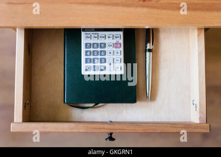 top view of pen, calculator and notebook in open drawer of nightstand Stock Photo