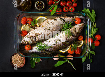 Two baked seabass in a baking dish with spices on an black background. Top view Stock Photo