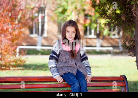 Beautiful little girl sitting on a bench in autumn park Stock Photo