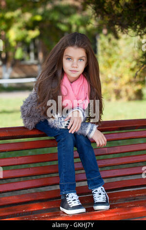 Beautiful little girl sitting on a bench in autumn park Stock Photo