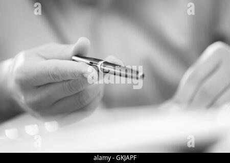 Man's hands holding a black pen in both arms in a thinking gesture during a meeting or negotiation.  Black and white image Stock Photo