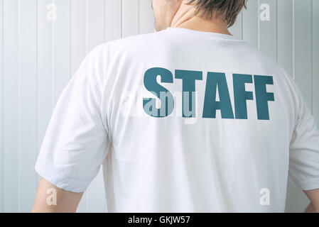 Man wearing white t-shirt with title Staff printed on back, member of employee team facing the wall Stock Photo