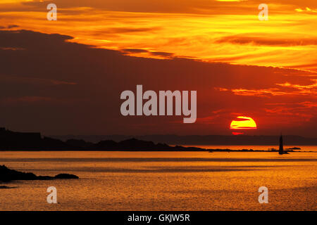 A big setting sun in the burning orange cloudy sky just over the sea with a lighthouse