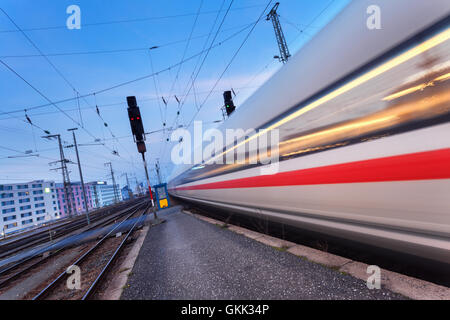 High speed passenger train on railroad track in motion at night. Blurred commuter train. Railway station at twilight