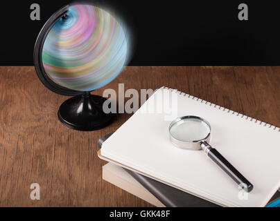 spinning globe and notebooks with a magnifying glass Stock Photo