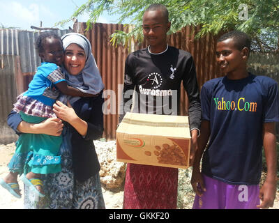 AMISOM's Woman & Child Protection Office, Kaoutar Kaddouri, holds a child after handing a box of dates to young men during a distribution of dates to less fortunate families around Mogadishu by the AMISOM Gender Unit on 3rd July 2014. The dates were given to the Unit by the Embassy of the United Arab Emirates. AMISOM Photo Stock Photo