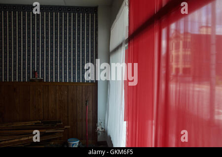 A red and white curtain in a windowsill with a striped wallpaper design Stock Photo