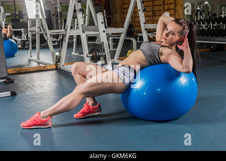 A muscular young women working out (or exercising) in a gym with an exercise ball Stock Photo