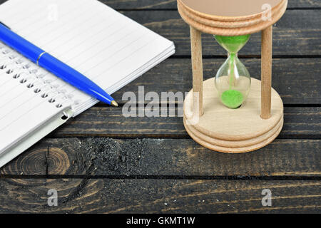 Hourglass and notepad close-up on wooden table Stock Photo