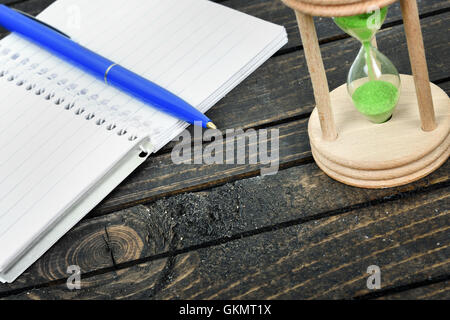 Hourglass and notepad close-up on wooden table Stock Photo