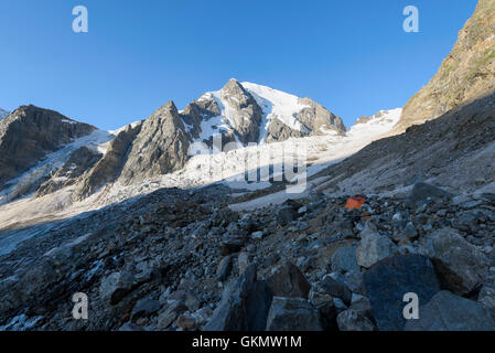 Orange tent among stones in highland camp against mountains and glaciers Stock Photo
