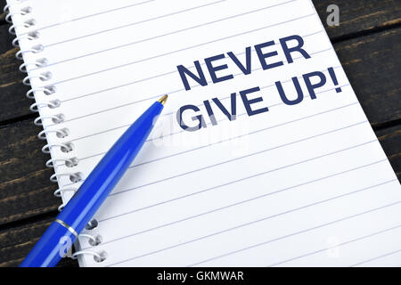 Never Give Up text on notepad and blue pen Stock Photo
