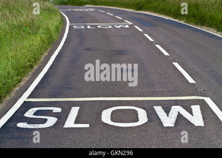 Three warning signs to slow down painted on a curving road Stock Photo