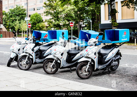 Line of Domino's Pizza Delivery Motor Scooters or Bikes Parked on the Side of the Road Stock Photo