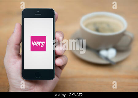 A man looks at his iPhone which displays the Very logo, while sat with a cup of coffee (Editorial use only). Stock Photo