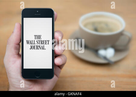 A man looks at his iPhone which displays the The Wall Street Journal logo, while sat with a cup of coffee (Editorial use only). Stock Photo