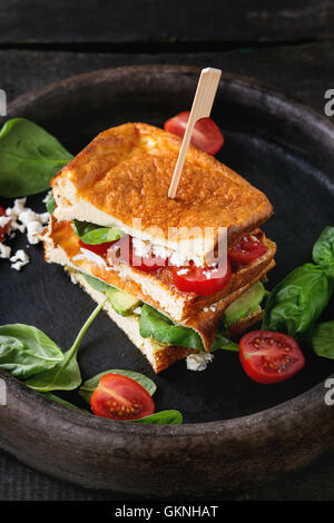 Low-carb gluten free Cloud bread veggie sandwich with spinach, avocado, feta cheese, tomatoes and pesto sauce, served on clay tr Stock Photo