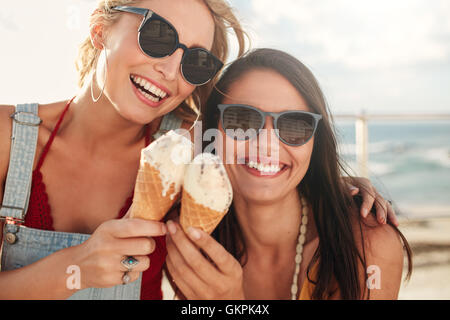 Shot of two young friends enjoying ice cream together on a summer day outdoors. Close up of cheerful female buddies eating icecr