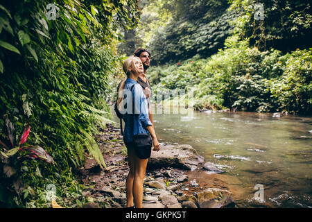 Outdoor shot of couple of tourist standing by a small stream in the rainforest. Hiker couple standing by stream in woods. Stock Photo