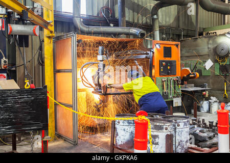 workman grinding and cutting away cast metal components from its 'casting' tree. Stock Photo