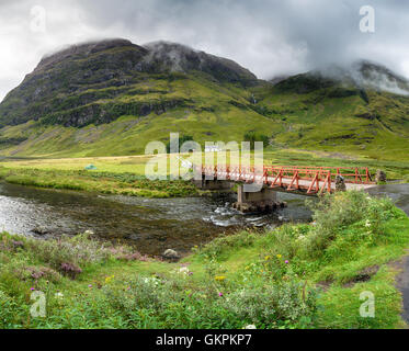 A bridge over the river Coe with Achnambeithach cottage nestled under the mountains Stock Photo