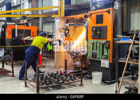 workman grinding and cutting away cast metal components from its 'casting' tree. Stock Photo