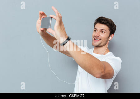 Casual young man making selfie photo on smartphone and listening music over gray background Stock Photo
